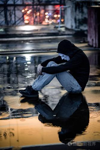 男人在白色面具下拥抱着他的膝盖坐在废弃建筑的屋顶上的雨中双相情感
