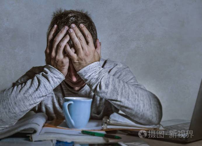 年轻的担心和沮丧的男人深夜工作在办公桌上手提电脑感到沮丧和疲惫