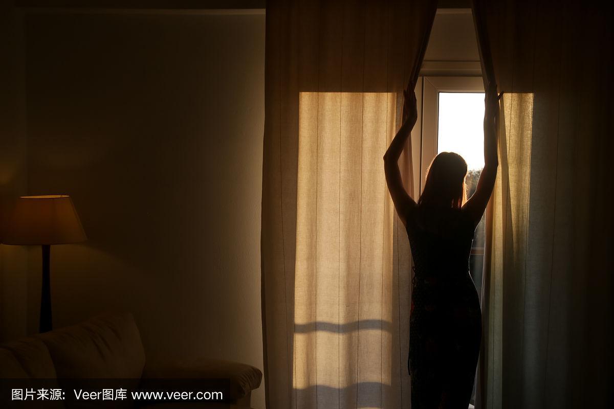 女人在一个阳光明媚的早晨拉开窗帘